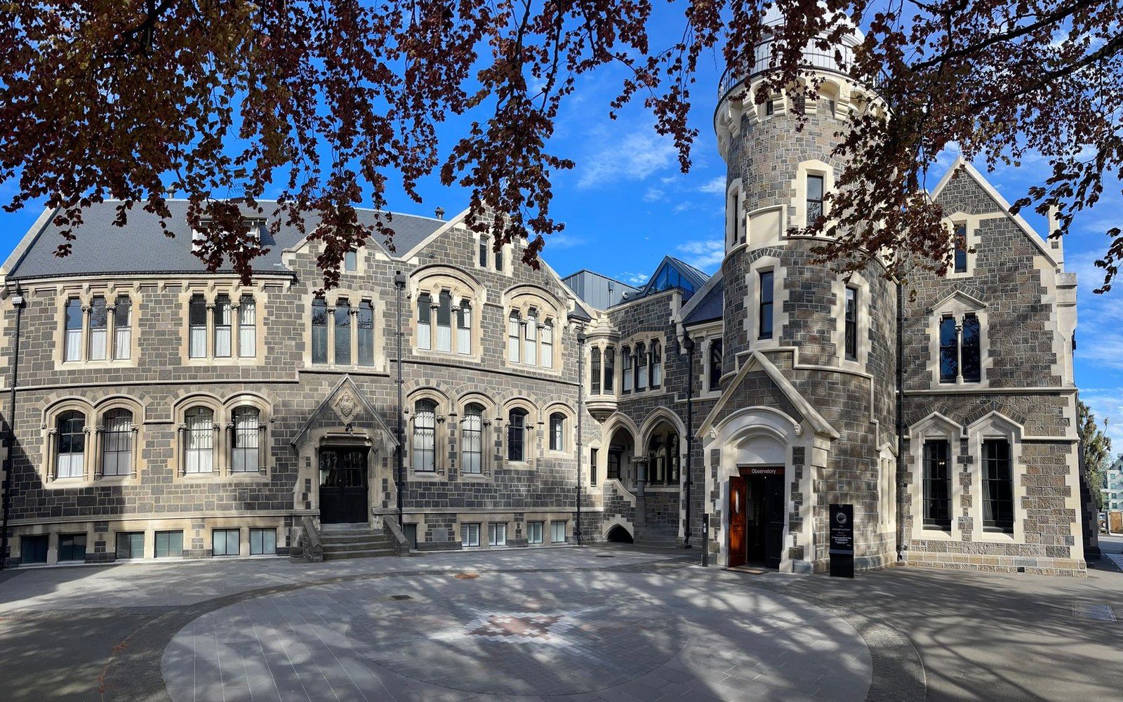 Stone gothic revival building with a round turret and arched windows under blue sky