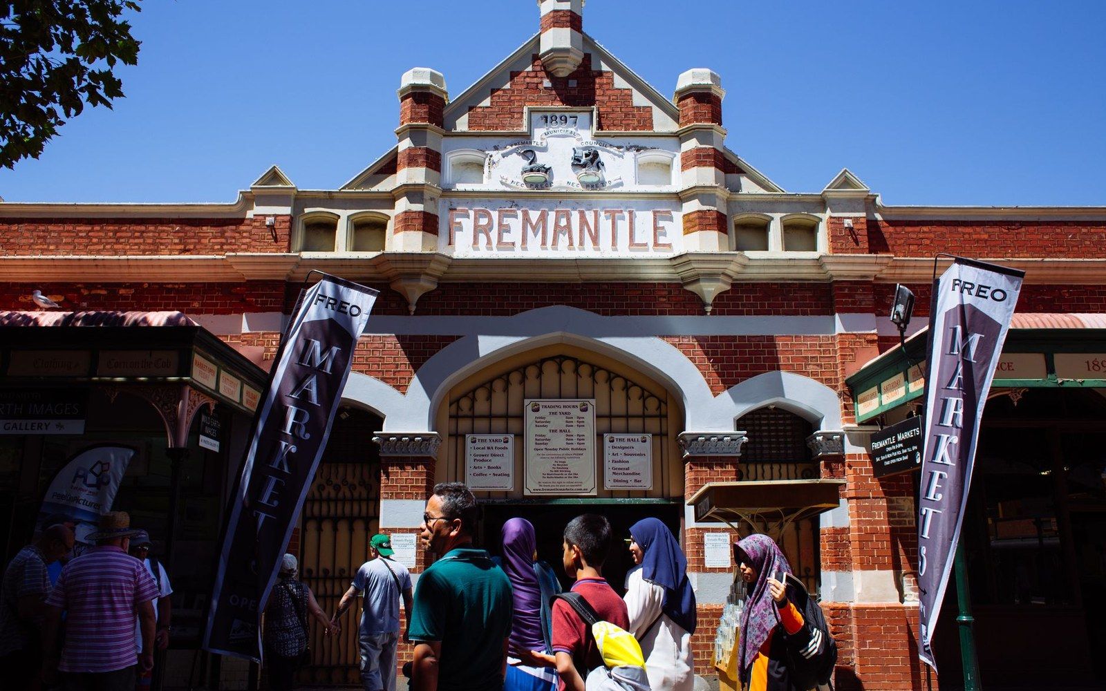 Visitors gather outside the historic brick facade of Fremantle Markets under a clear blue sky