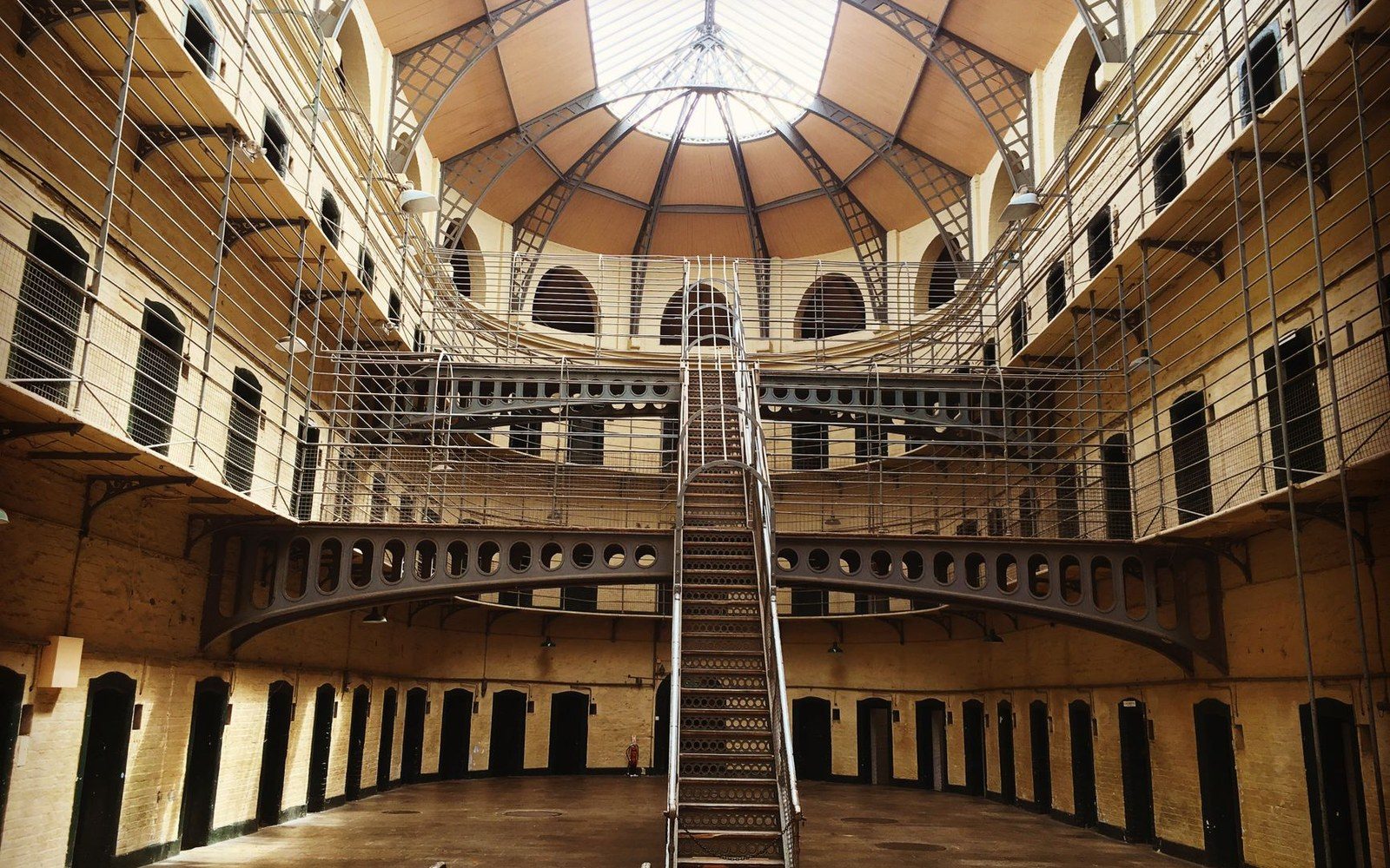 Tiered cell blocks and iron staircase inside a domed prison hall with skylight