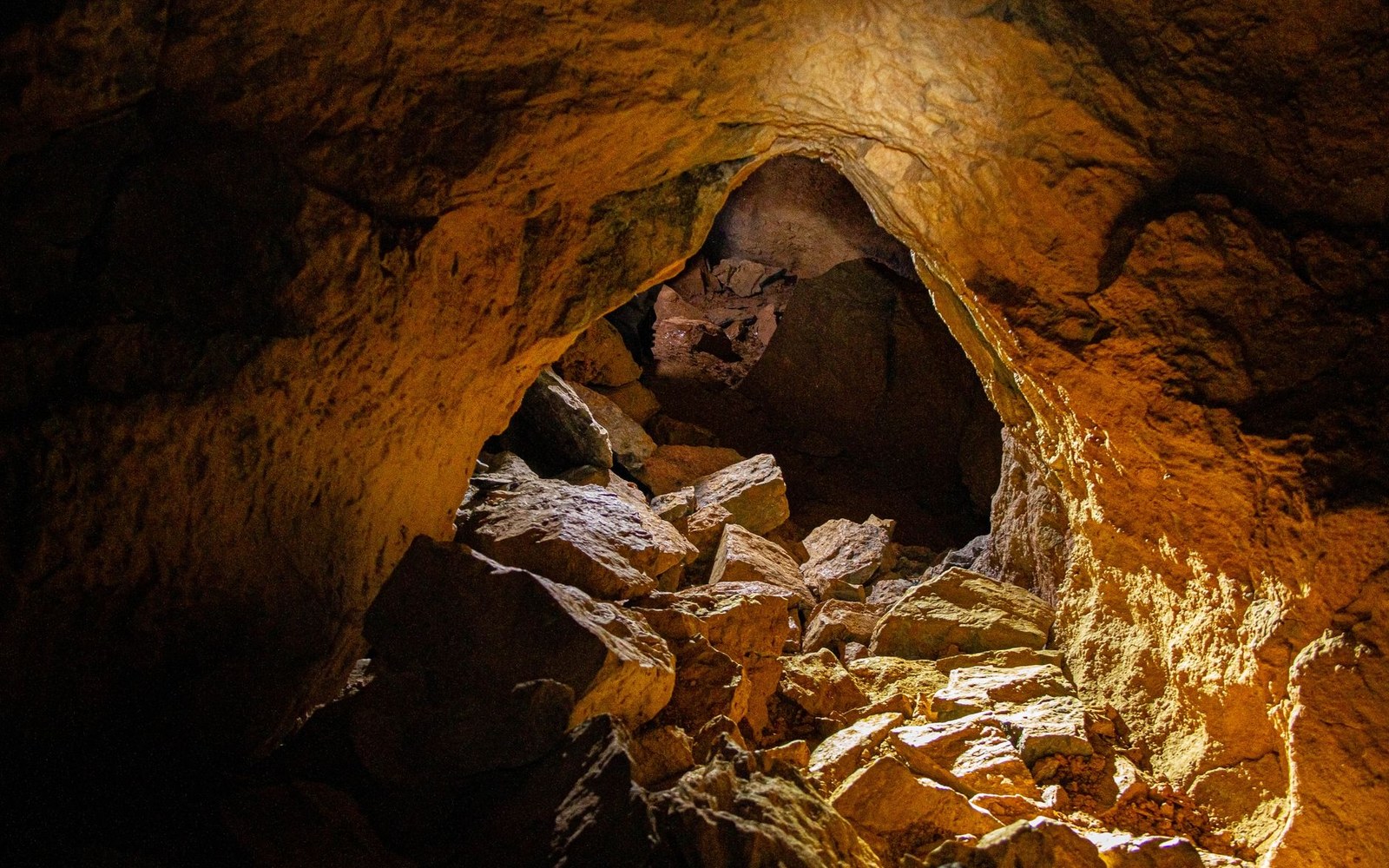 Rocky tunnel interior with rubble-strewn floor lit by warm overhead light