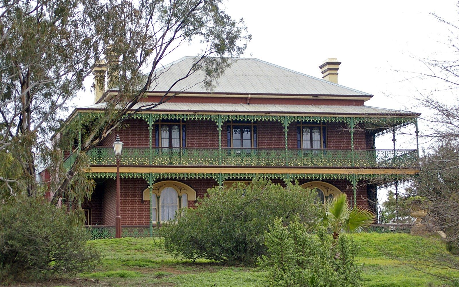 Monte Cristo Homestead's iron-lace verandah photographed in flat midday light, the homestead's facade behind it